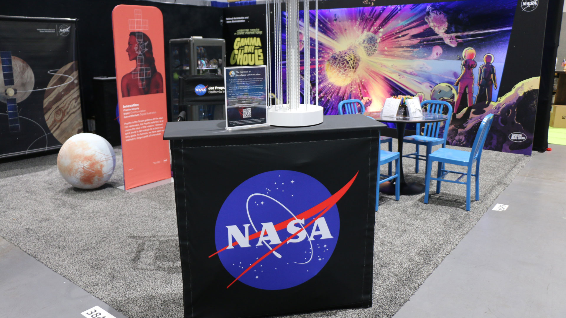 une étagère noire avec le logo bleu de la NASA sur un tapis gris au sol d'un salon de bande dessinée