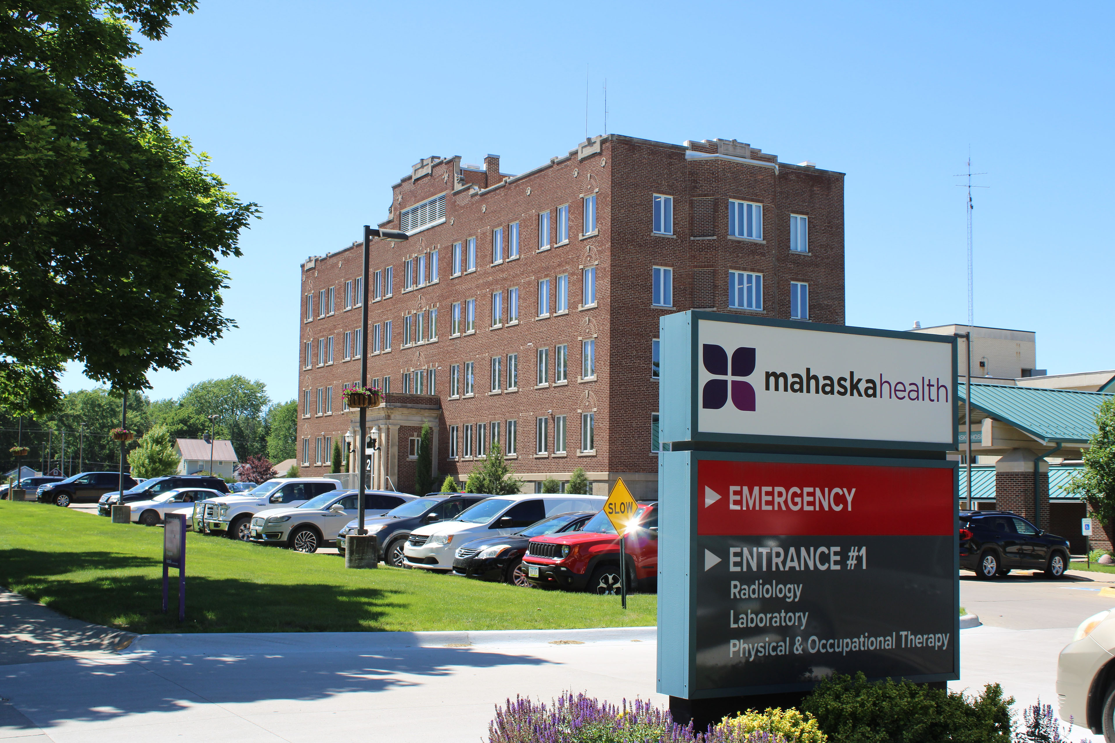 L'extérieur de l'hôpital Mahaska Health. C'est un bâtiment en briques avec un parking et une pelouse verte devant. Un panneau d'entrée est situé à droite.