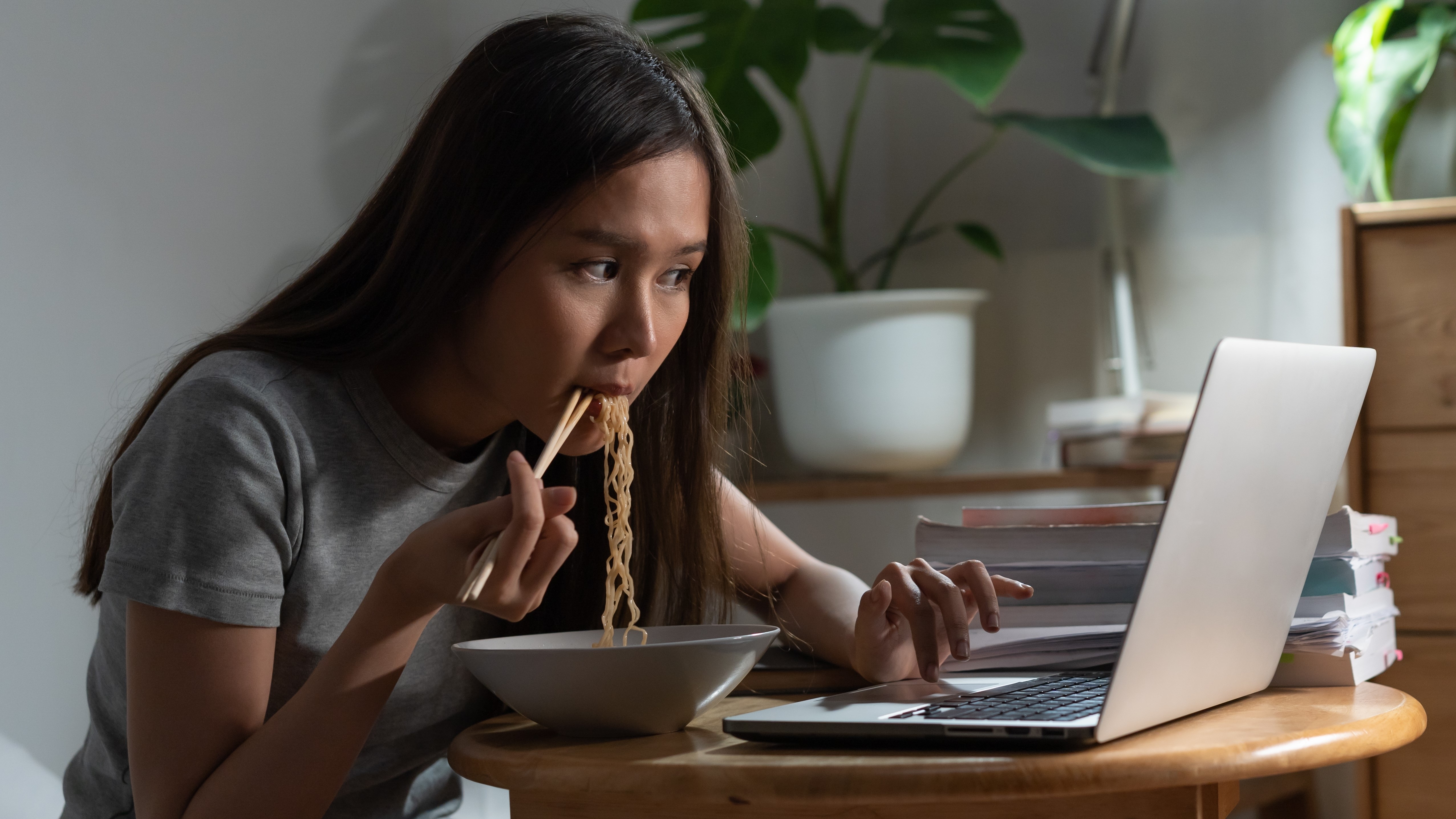 Une femme assise à une table, mangeant des ramen et interagissant avec un ordinateur portable