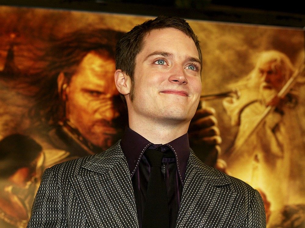 médecine Elijah Wood se tient devant un poster du Seigneur des Anneaux avec Aragorn (Viggo Mortensen) et Gandalf (Ian McKellen).