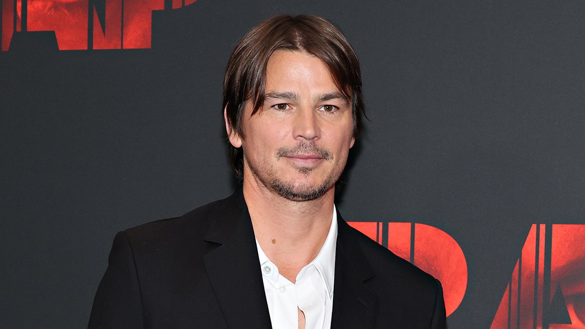 L'acteur Josh Hartnett sourit en portant un costume noir et une chemise blanche.