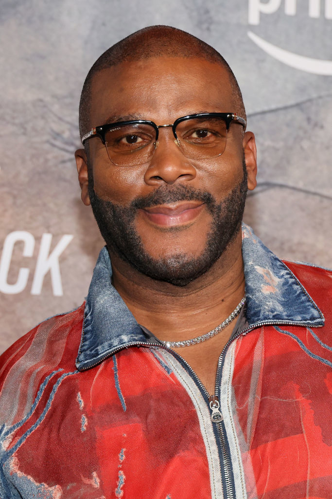 Tyler Perry souriant sur le tapis rouge dans une veste à motifs élégante et des lunettes à monture transparente