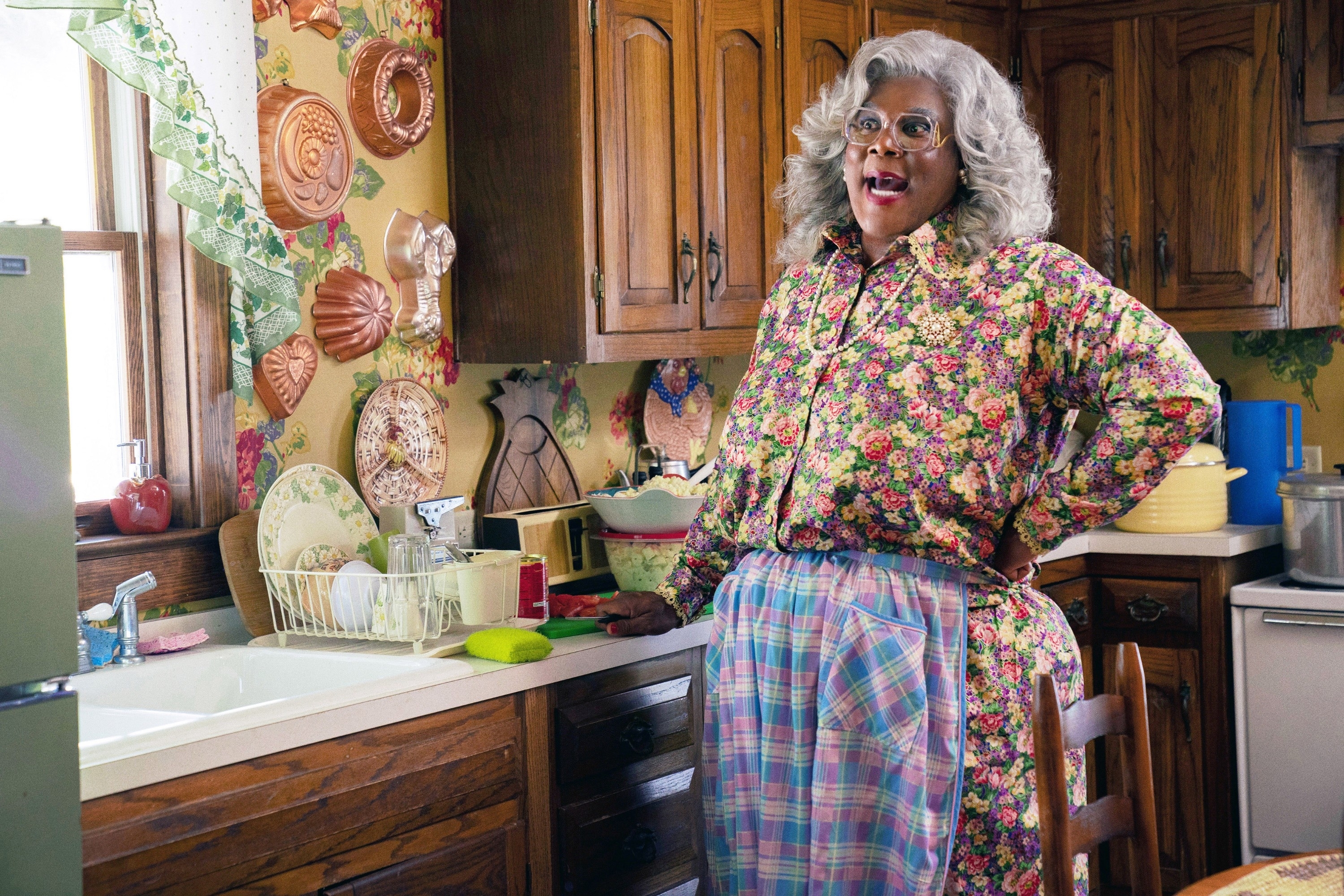 Madea dans une cuisine portant un chemisier fleuri et un tablier à carreaux