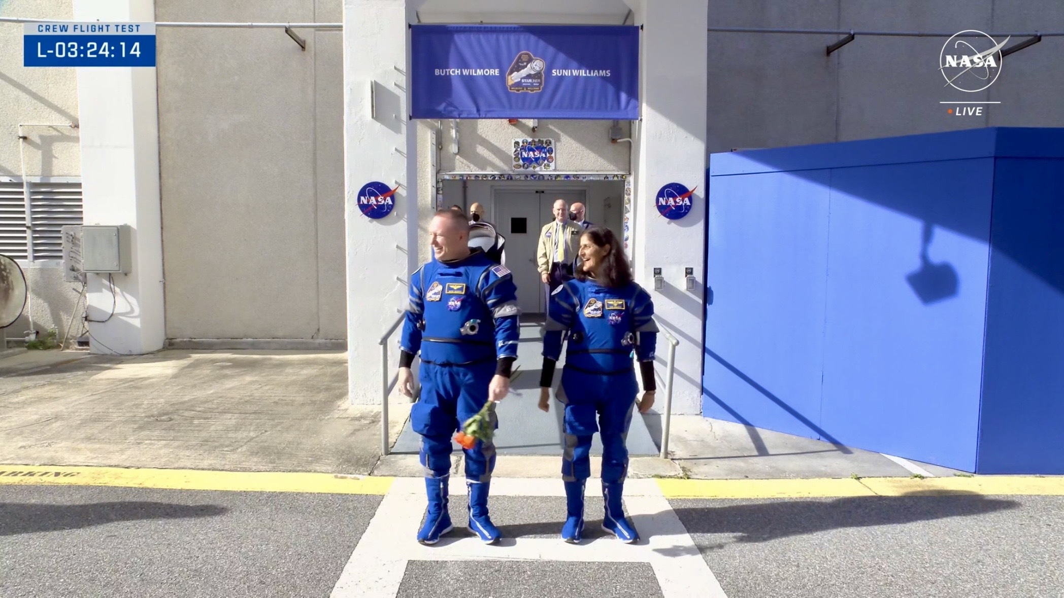 science deux astronautes en combinaisons bleues se tiennent devant deux piliers avec des logos NASA.