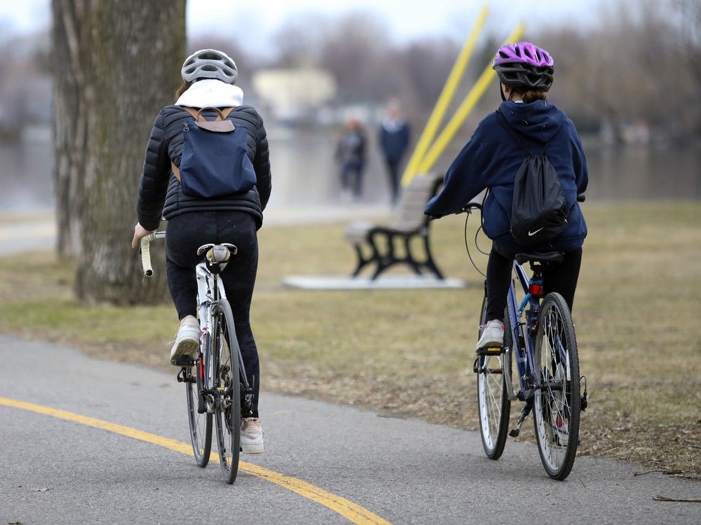 actualité Deux cyclistes roulent côte à côte sur la piste cyclable le long de la rivière à Lachine.