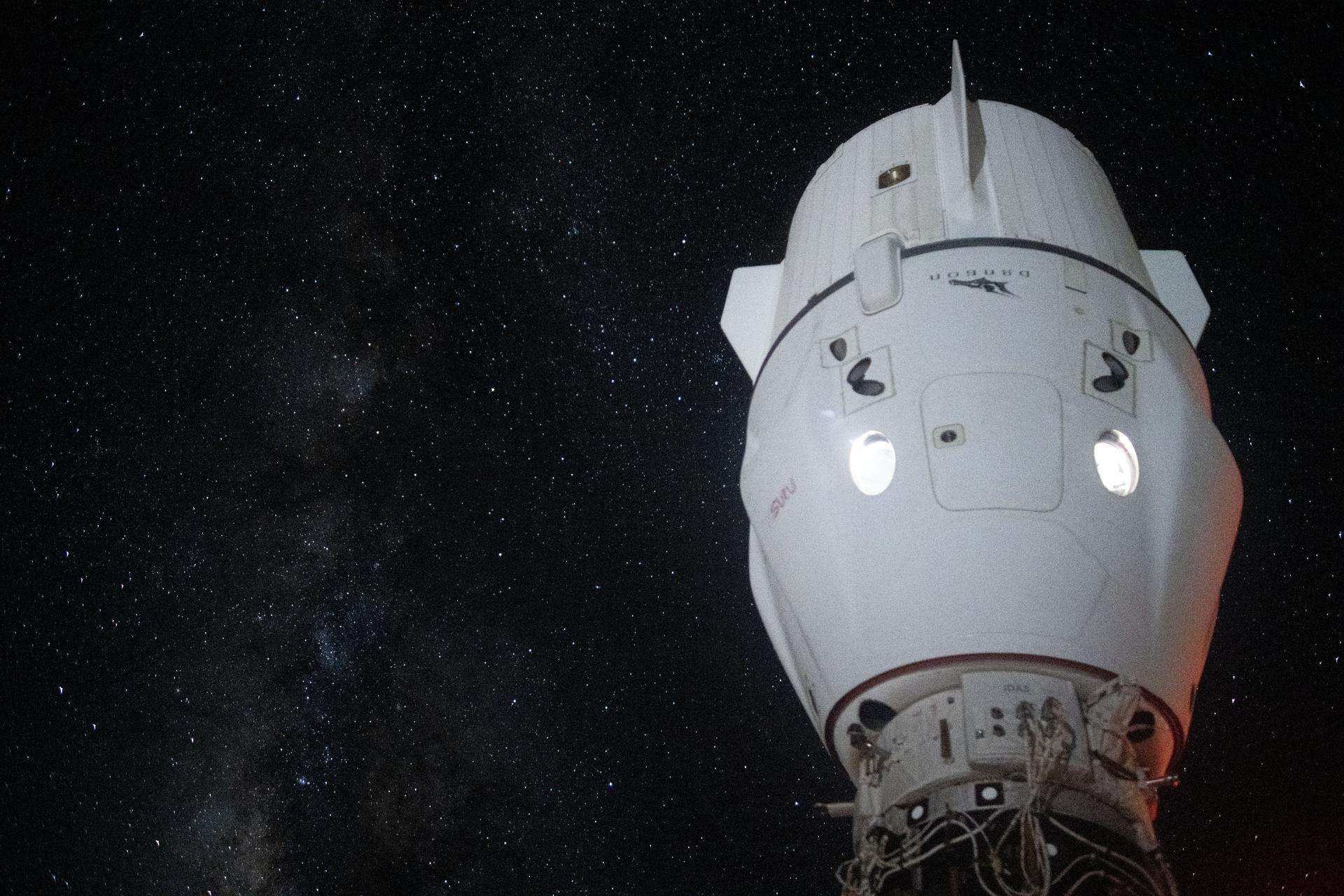 science Un vaisseau spatial blanc accosté à la Station spatiale internationale, avec la Voie lactée en arrière-plan.