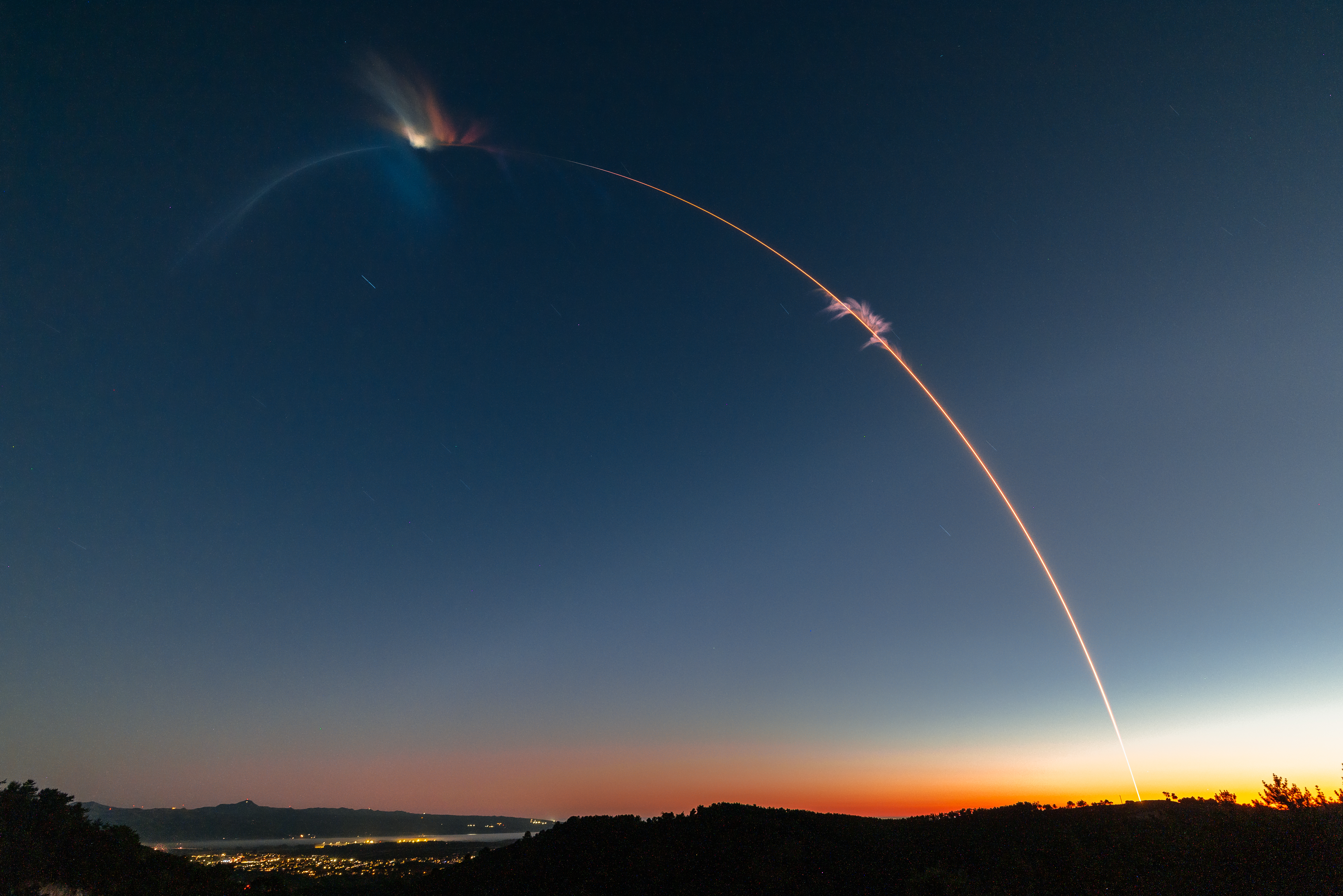 science une fine traînée de lumière orange traverse un ciel sombre, émergeant de l'horizon bas à droite, où le ciel brille d'orange.