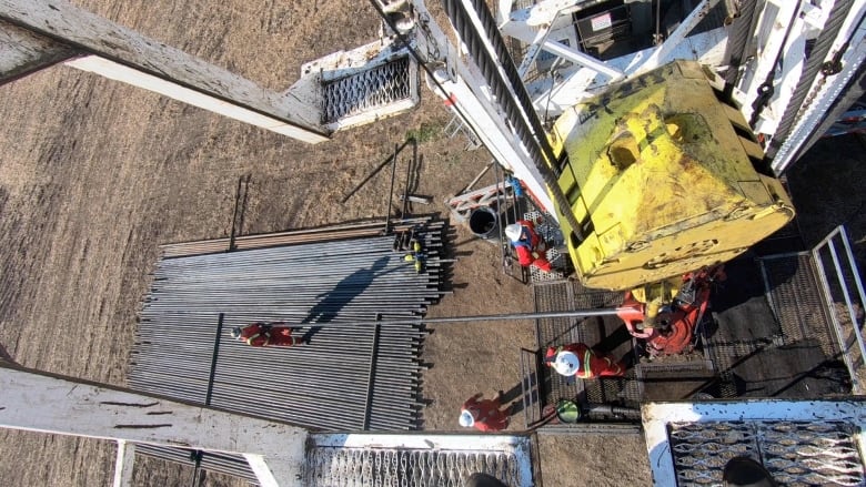 actualité A top down view of workers in red suits and white helmets doing work on a large piece of yellow metal industrial equipment.