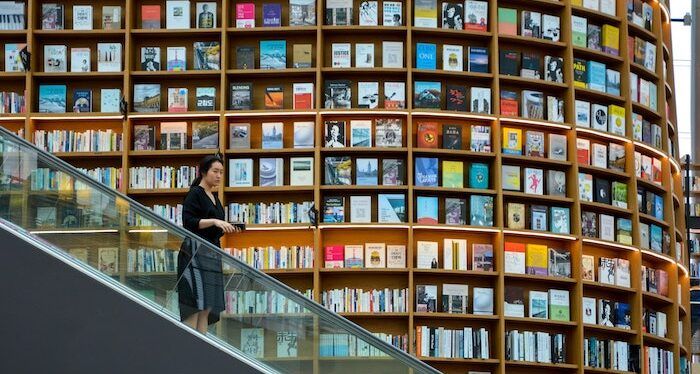 actualités une personne descendant un escalator avec d'énormes étagères de livres en arrière-plan s'étendant sur les deux étages